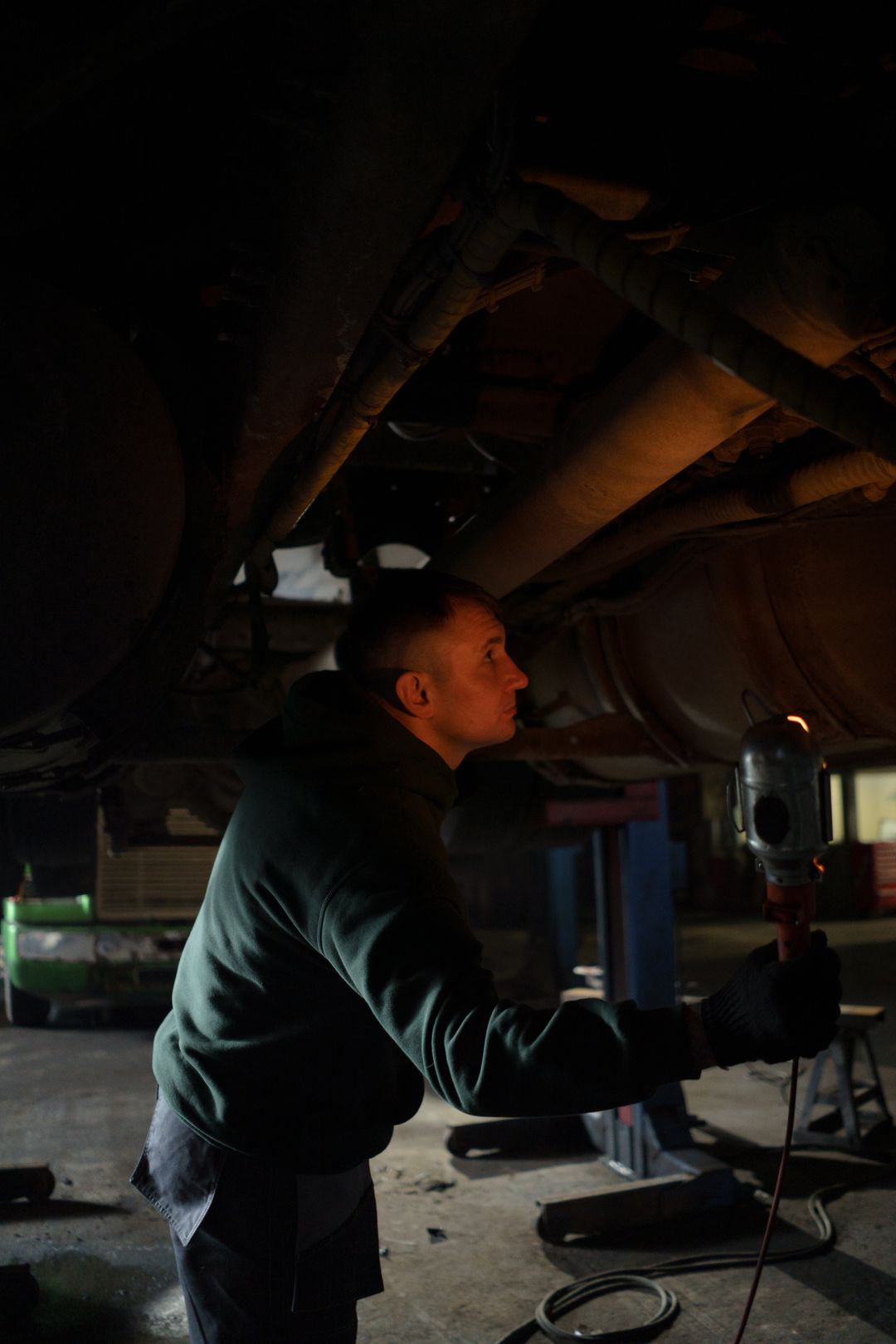 Mechanik z lampą warsztatową sprawdza podwozie auta na podnośniku